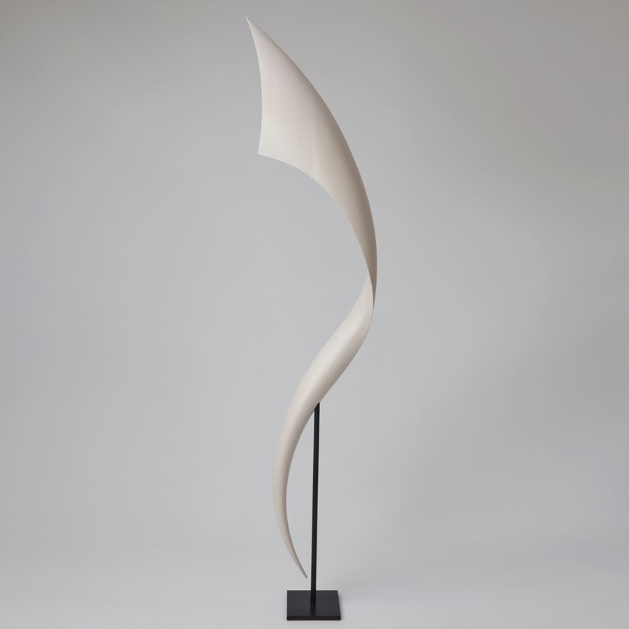 tall standing curved flaring white wooden sculpture with narrow base widening towards to the top and as it curves around presented on a black steel simple stand