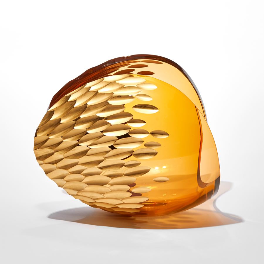 rich amber peach transparent ovoid sculpture with sweeping cut away section creating a curved traversing rim with repeat leaf shaped patterned incised section in gold hand made from glass