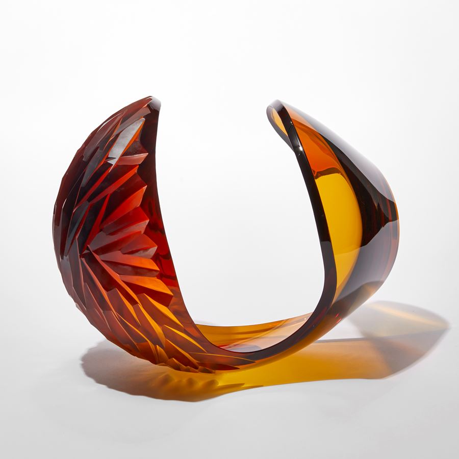 transparent dark rich amber laid down egg shaped sculpture with large cut away section leaving a sweeping curved edge with repeat diamond pattern cut area hand made from glass