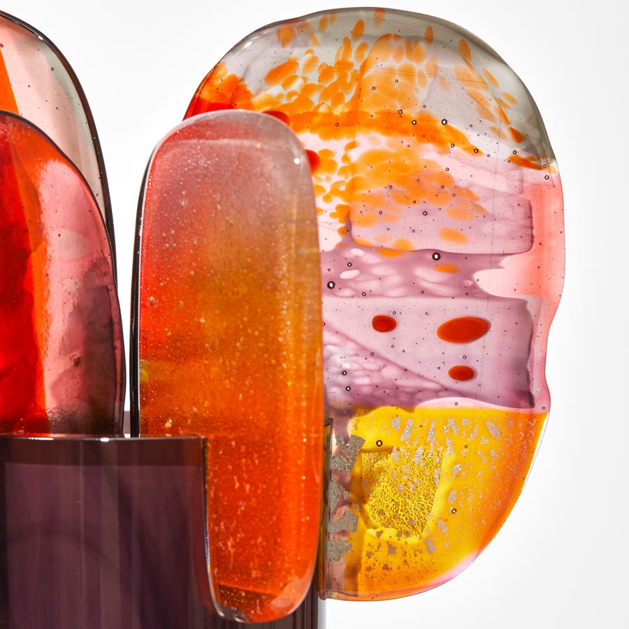 tall opaque shiny rich brown coloured cylinder with 5 rounded finials perched on the top rim in a dazzling array of colours pink yellow red orange and grey with abstract dots and patterns hand made from glass
