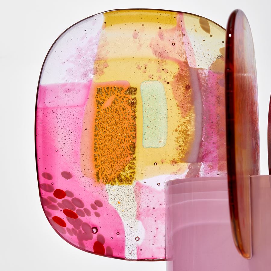 rich shiny opaque pink cylinder with colour fade towards the top with five finials overlapping the top edge each with abstract patterns in pink yellow and gold hand made from blown and fused glass