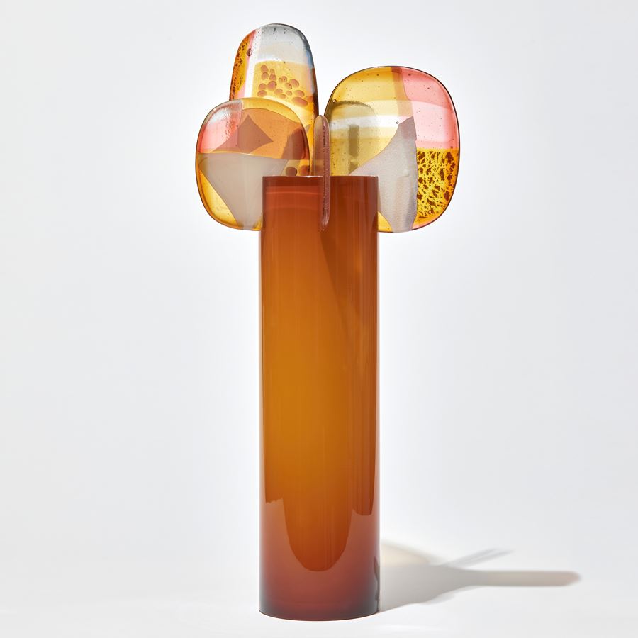 opaque burnt orange shiny cylinder with rounded fins in pink yellow gold pink and grey with abstract patterns perched on the top handmade from glass