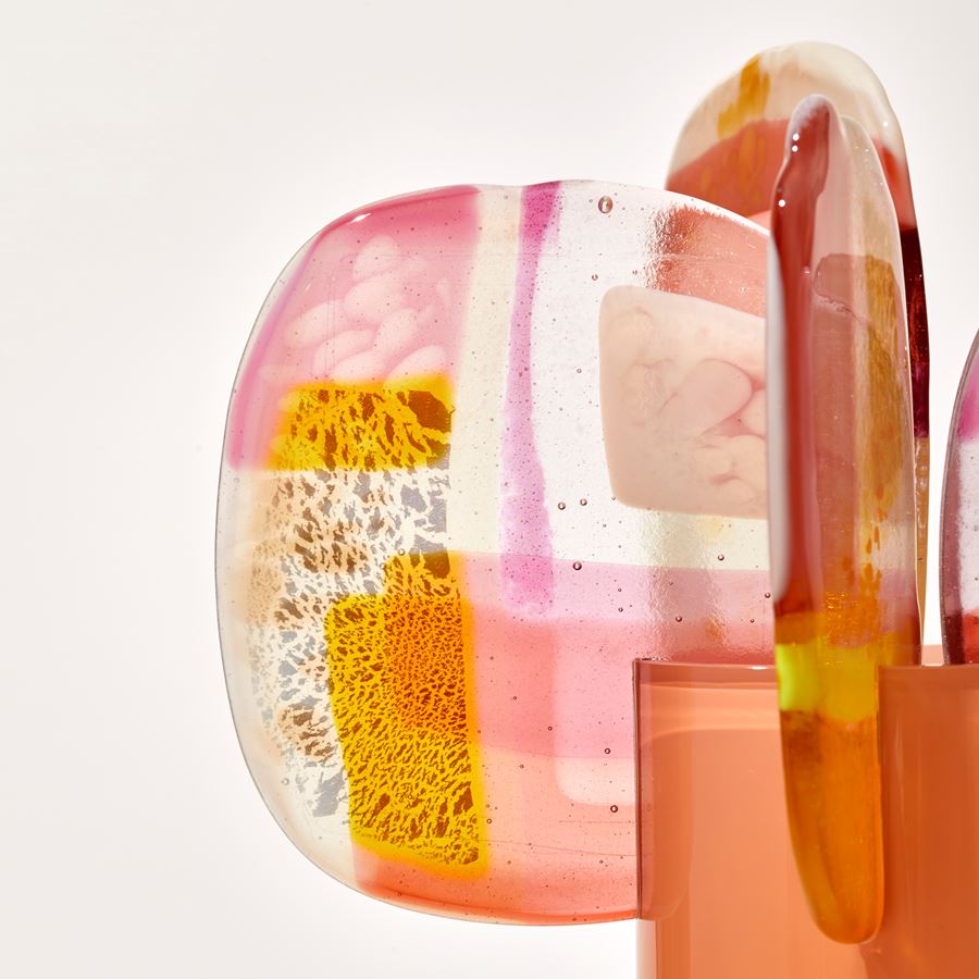 opaque peachy orange cylinder with colour fade from top to bottom and five rounded petals overlapping and perched on the top rim with abstract patterns in pink peach orange yellow white and clear handmade from blown and fused glass
