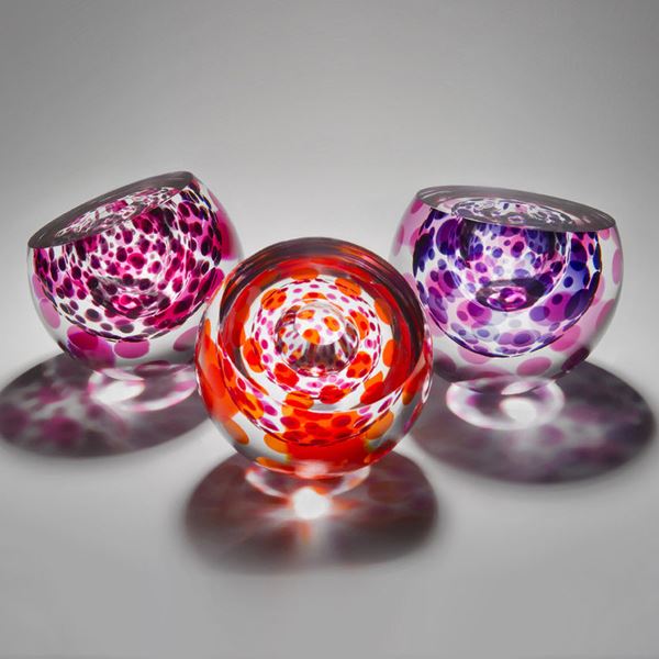 three rounded art glass sculptures in purple and red