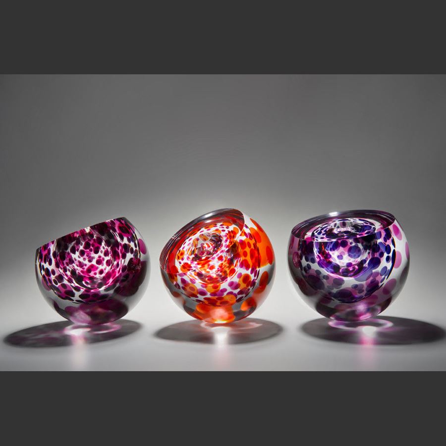 three rounded art glass sculptures in purple and red