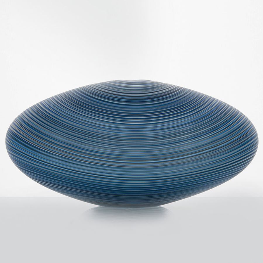 rounded zeppelin shaped glass sculpture with fine line patterned exterior in different shades of blue and grey