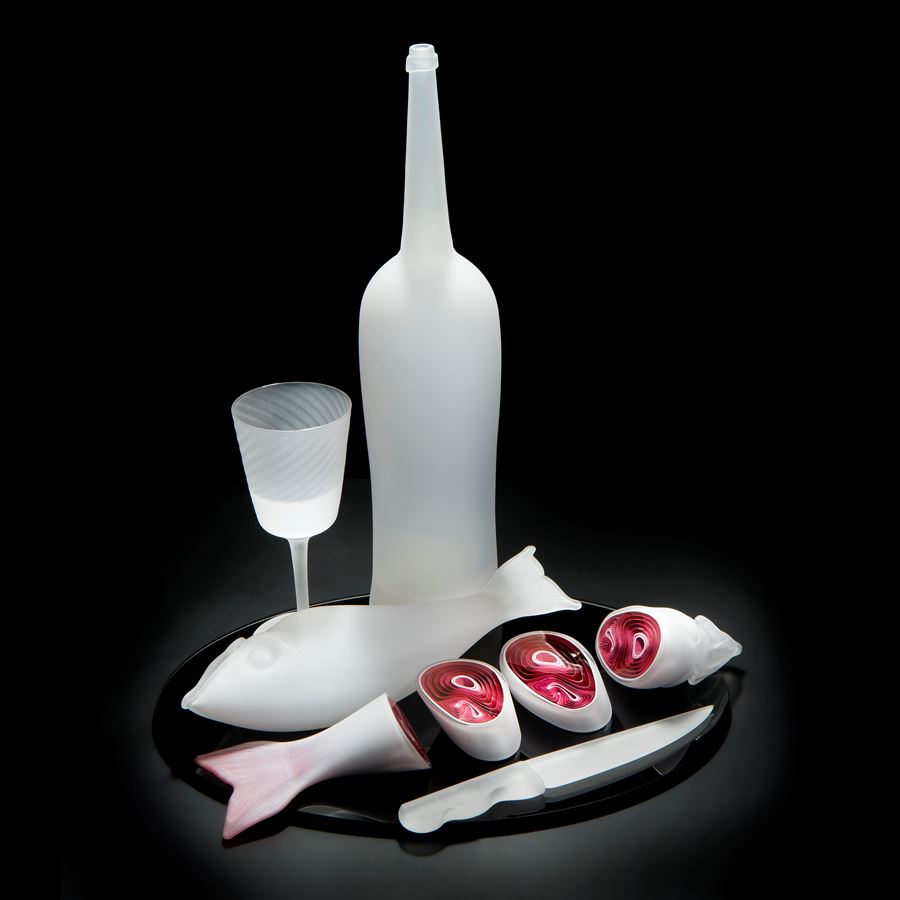 still life blown and sculpted glass art piece of cut fish, knife, bottle and glass in white
