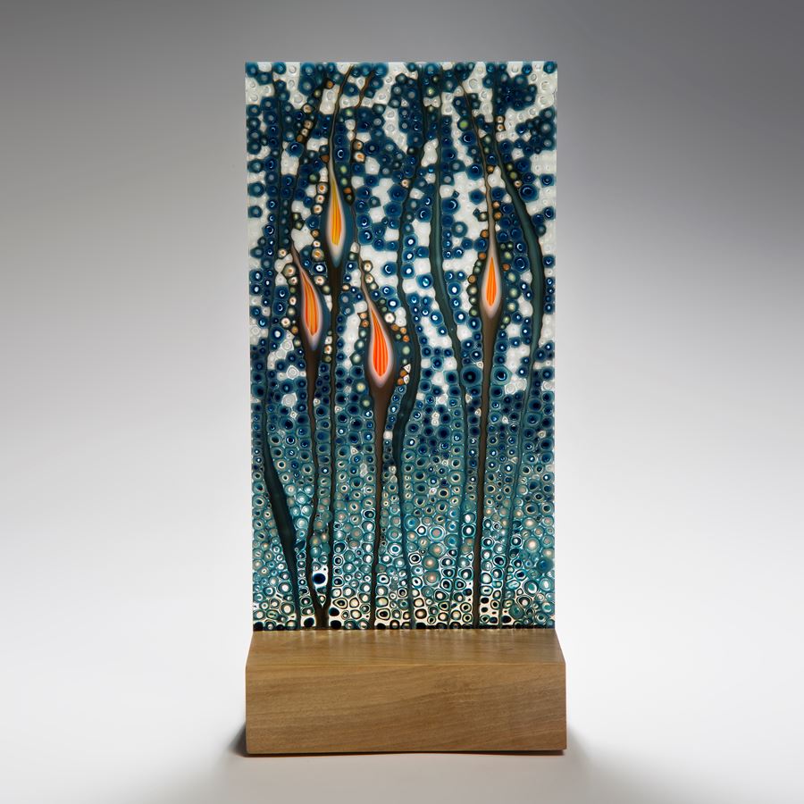 art glass sculptural panel in blue green and orange resting on wooden block