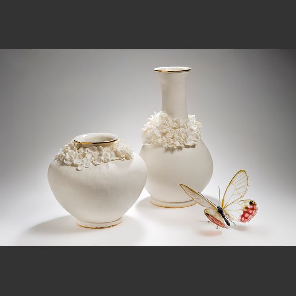 white ceramic vase with wide base and long neck and sculpted flowers