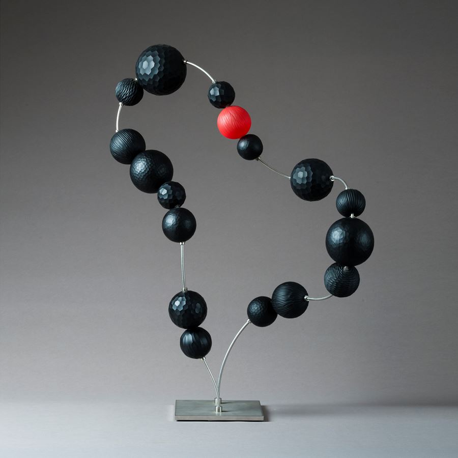 sculpted glass beads in black with one red bead laid out in abstract necklace form on metal base and thread
