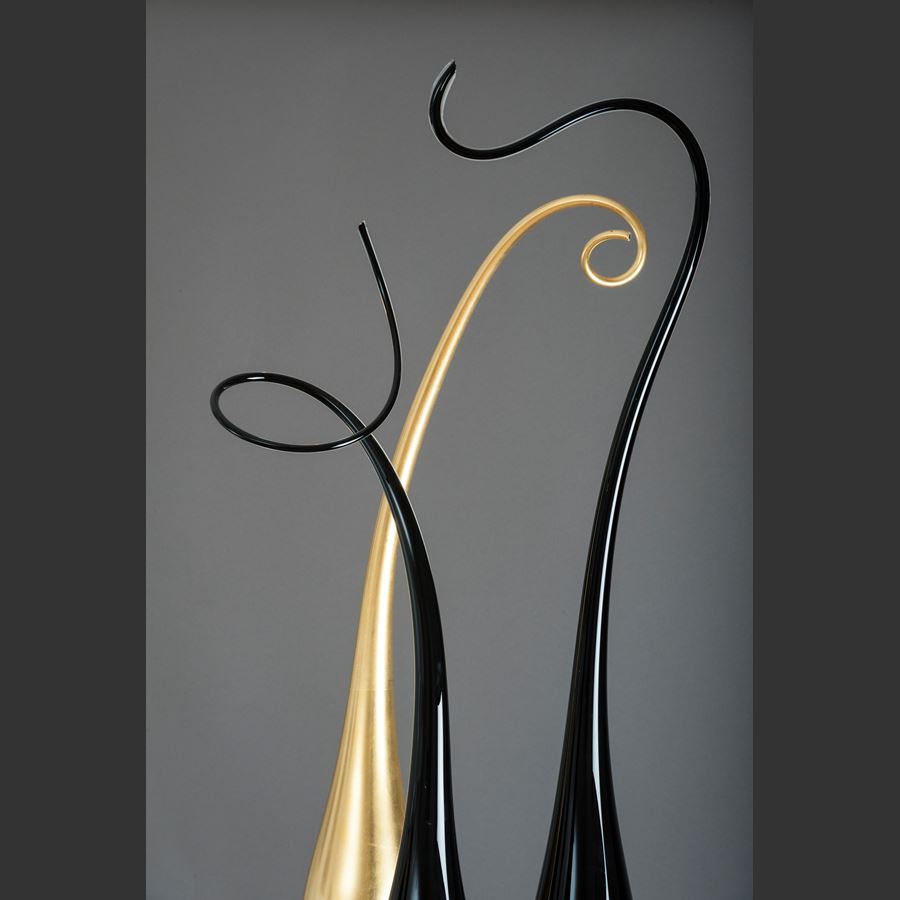three tall thin glass art strands in black and gold on steel stick bases