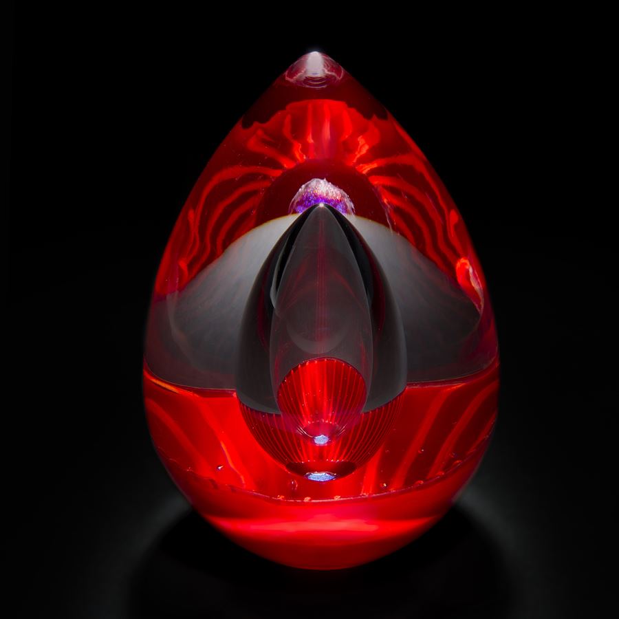 futuristic looking art glass sculpture in oval shape with bright reds and dark grey