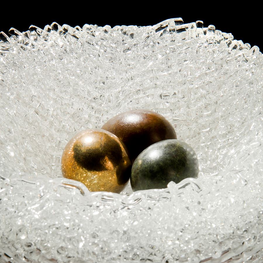 experimental kiln formed art glass sculpture resembling birds nest with three bronze eggs in centre
