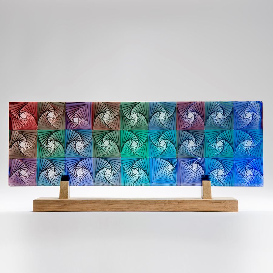 colourful flat rectangular cast glass sculpture resting on wooden base