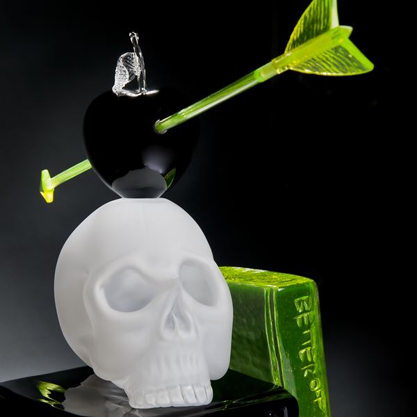 art glass still life sculpture of white skull on black base with neon green arrow through black apple resting on top