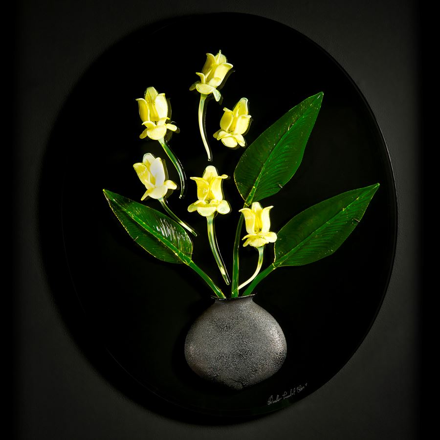 art glass wall sculpture of green leaves and yellow flowers in grey vase with black background