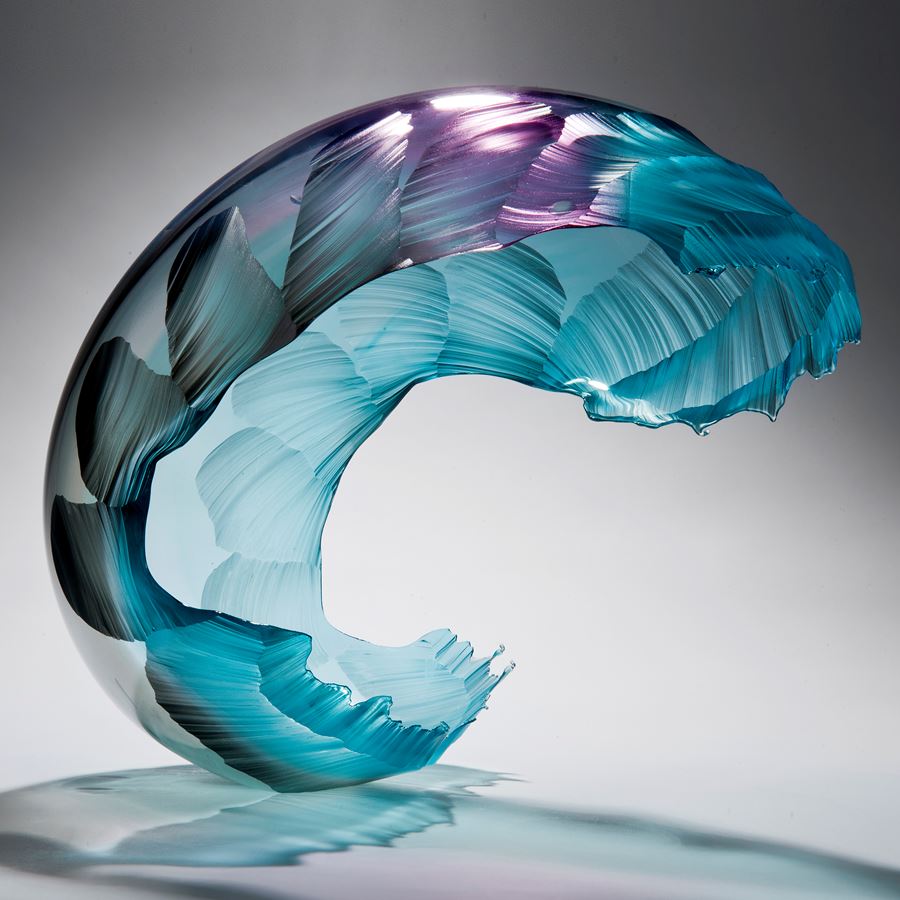 glass art sculpture in form of a wave in bright aqua blue with purple tint