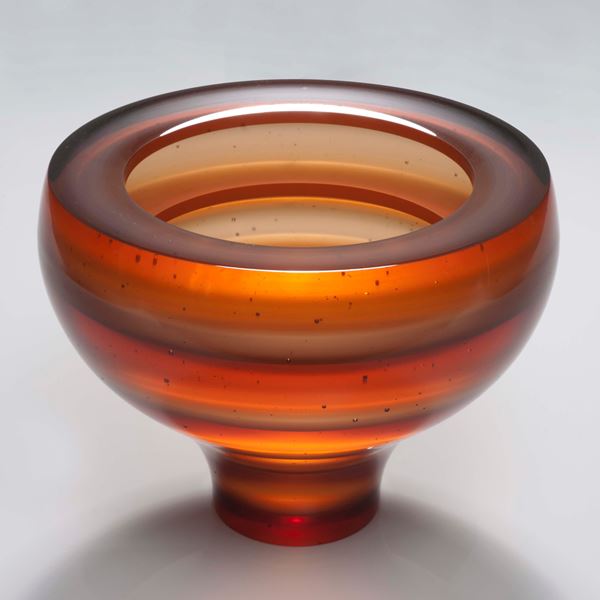 sculpted glass vessel with thin base and wide top with horizontal lined patters in orange shades