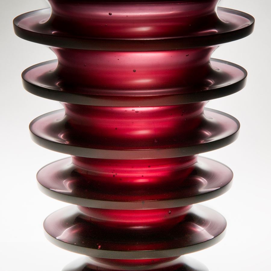 tall dark red art glass sculpture with geometrically positioned rings