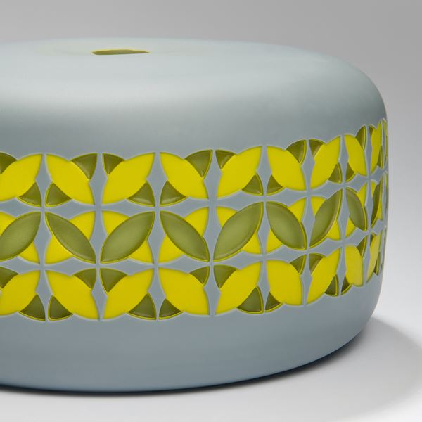 round cake shaped glass sculpture in grey with yellow and gren pattern