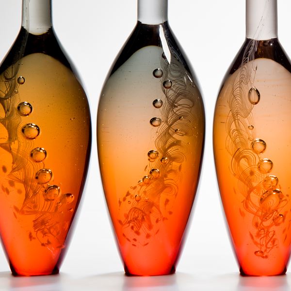 five bright orange modern glass vase sculptures with tall grey necks and engraved pattern