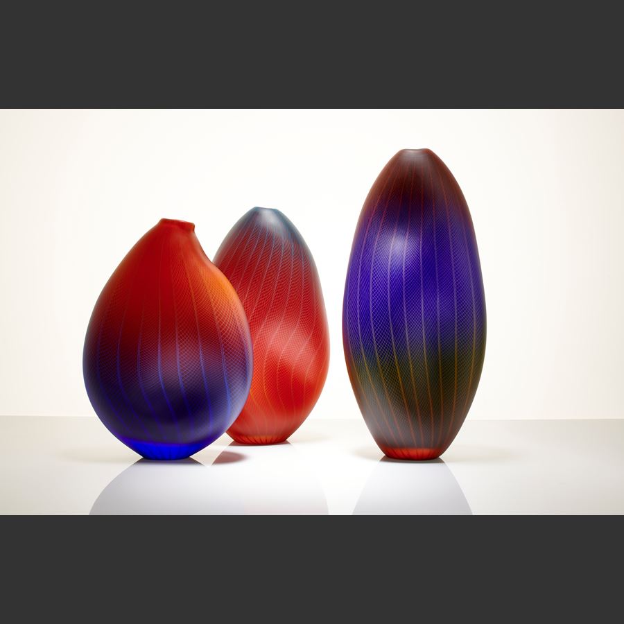 sculpted glass vessel in blue red and orange with small open top and lined and checked external engraved pattern
