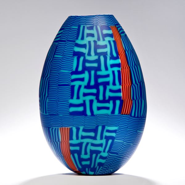 sculpted glasss vessel in oval shape with lined patterns in blue turquoise and orange