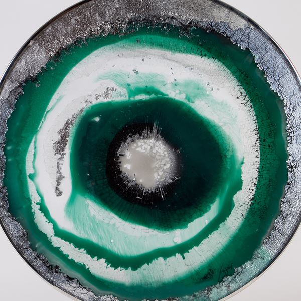 glass and steel sculpted circle with green silver and black swirls forming pattern of an eye