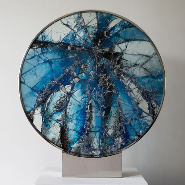 round glass art sculpture made from fragmented pieces in shades of deep blue to white and black resting on stainless steel bezel