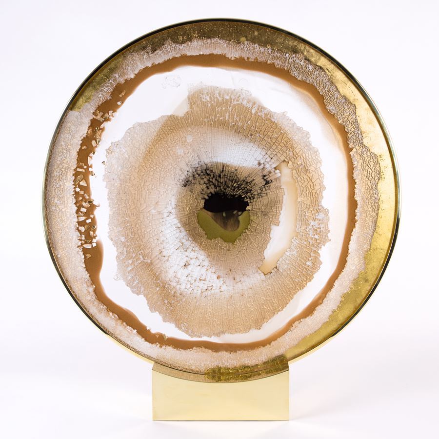 round glass art sculpture in earthy white yellow brown and gold resembling pattern of an eyeball sat on steel bezel