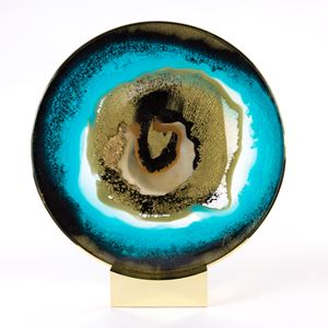 round glass sculpture with eye like qualities atop brass bezel and stand