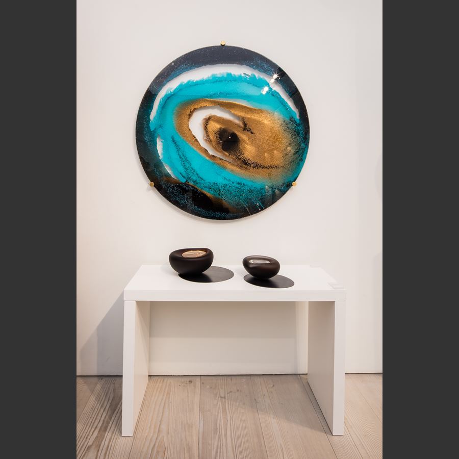 round glass art sculpture of eye-like shape in shades of blue and sand