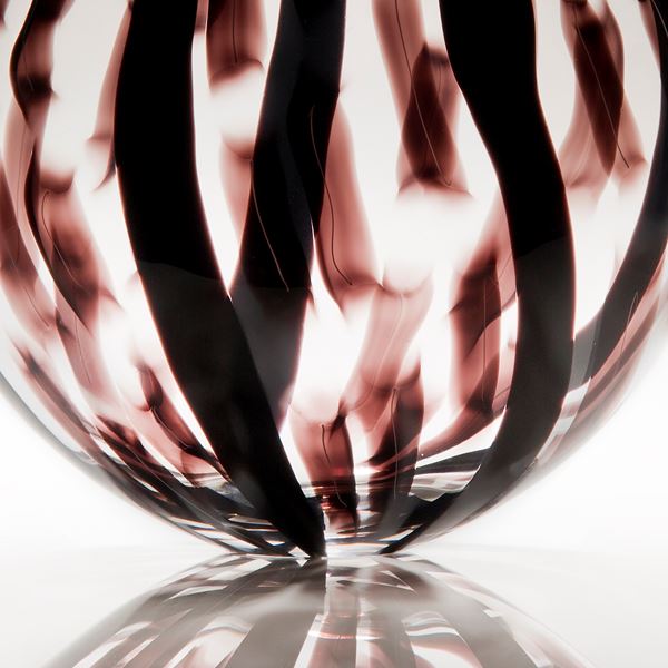 sculpted glass vessel with round base and short neck with black and dark red lined patterns