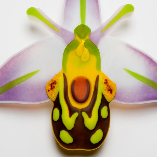 handmade fused glass sculpture of a bee nestling in an orchid in green orange white and purple