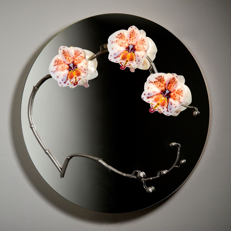round black glass mirror with three sculpted glass orchids