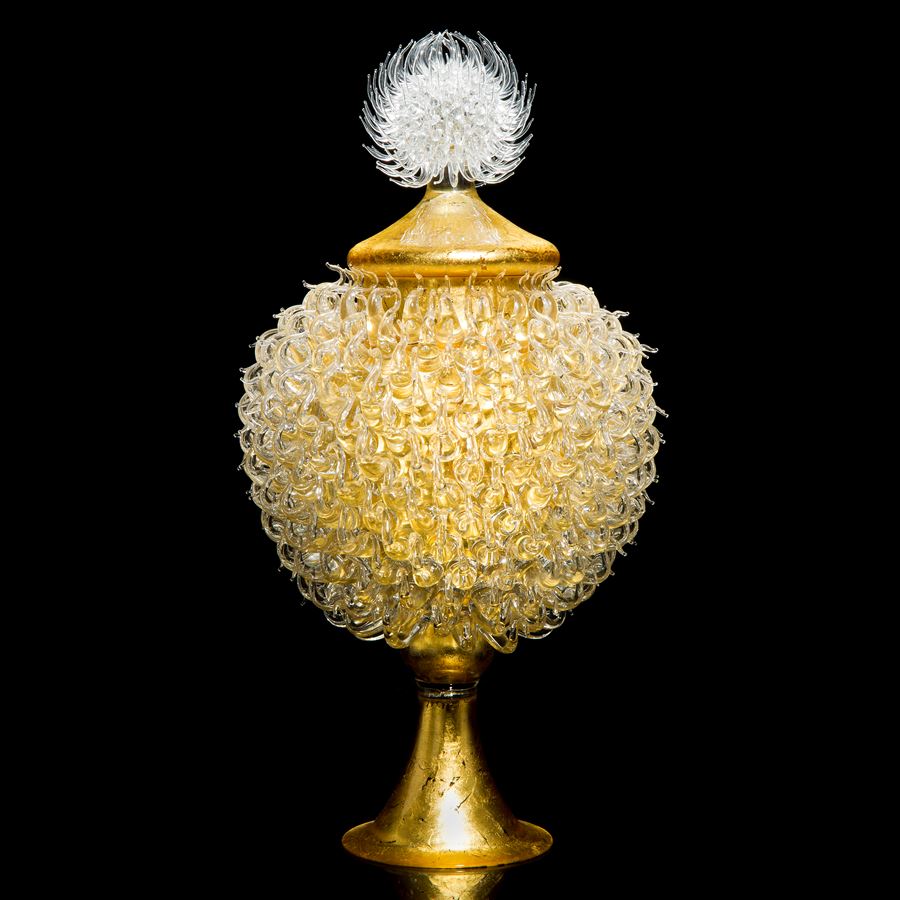 gold glass sculpture of round jar atop cone shaped base with white thistle top 