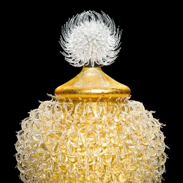 gold glass sculpture of round jar atop cone shaped base with white thistle top 