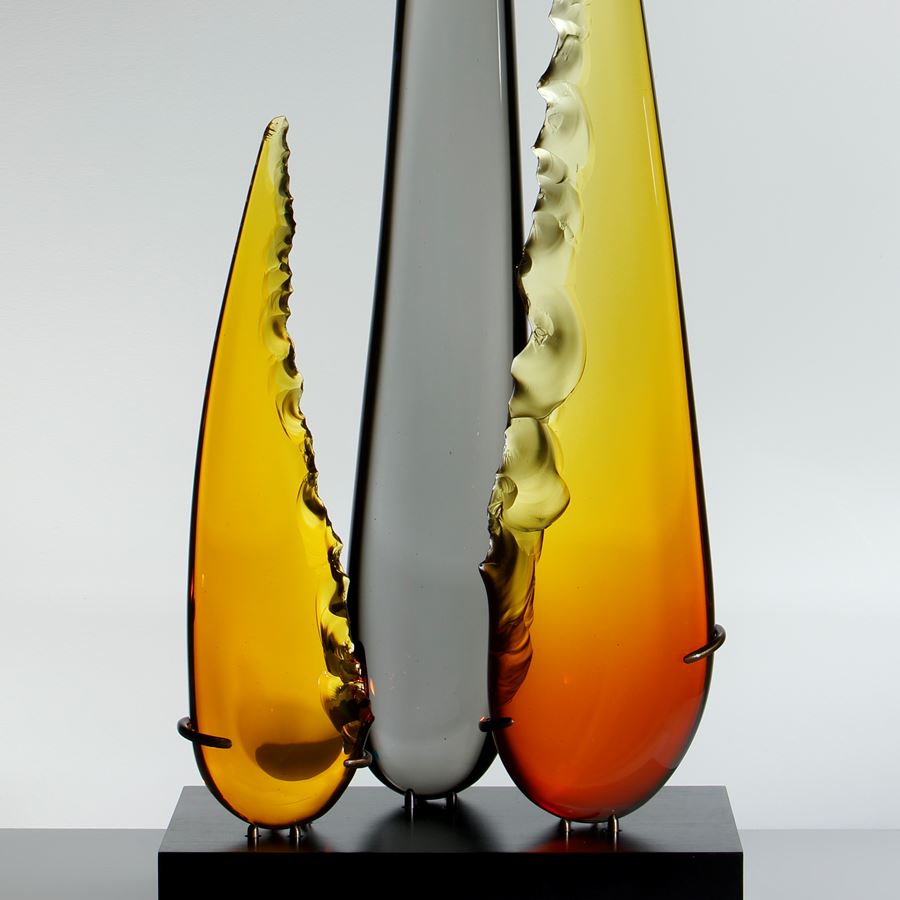 a trio of glass shards one long carbon coloured and centre flanked by two shorter amber and yellow shards resting on black metal base