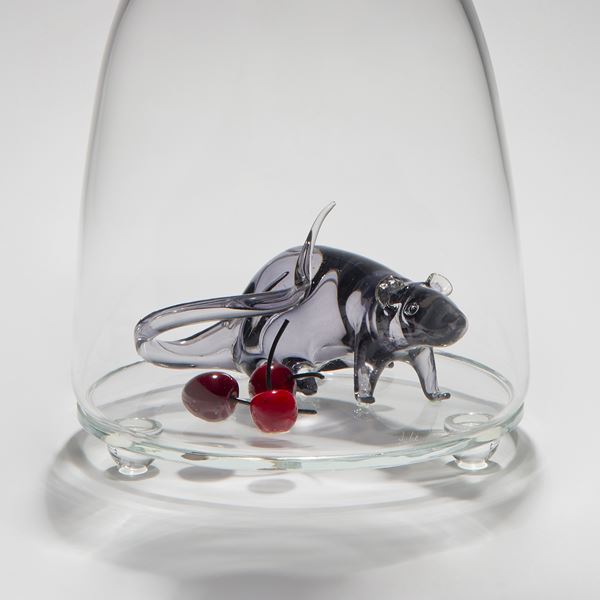 glass and steel sculpture of a mouse trapped in a clear glass flask with a crow peering in from the top