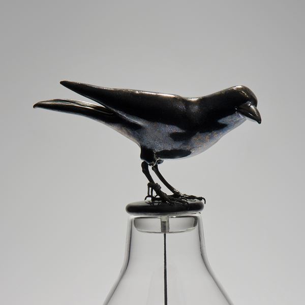 glass and steel sculpture of a mouse trapped in a clear glass flask with a crow resting on top