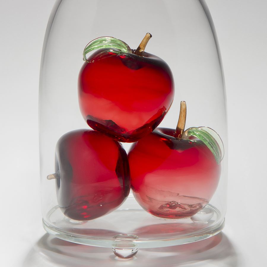 glass and steel sculpture of three apples inside glass container with a crow peering on top looking in