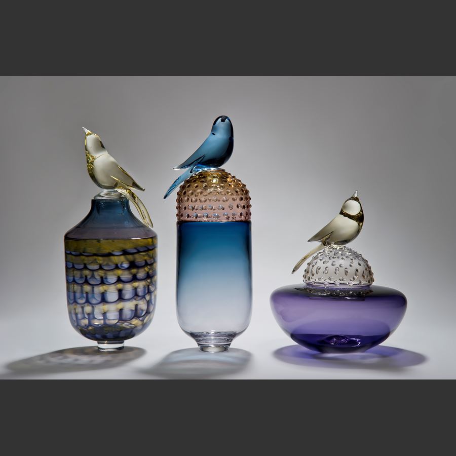 glass artwork of bird sat on top of funeral urn in blue purple yellow and gold