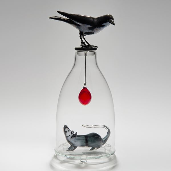 glass and steel sculpture of a mouse trapped in a clear glass flask with a crow resting on top