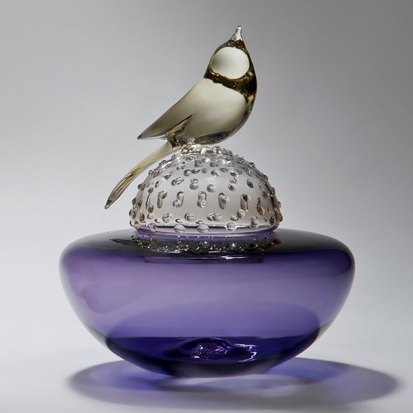 glass artwork of a light grey bird resting on a bright purple funeral urn