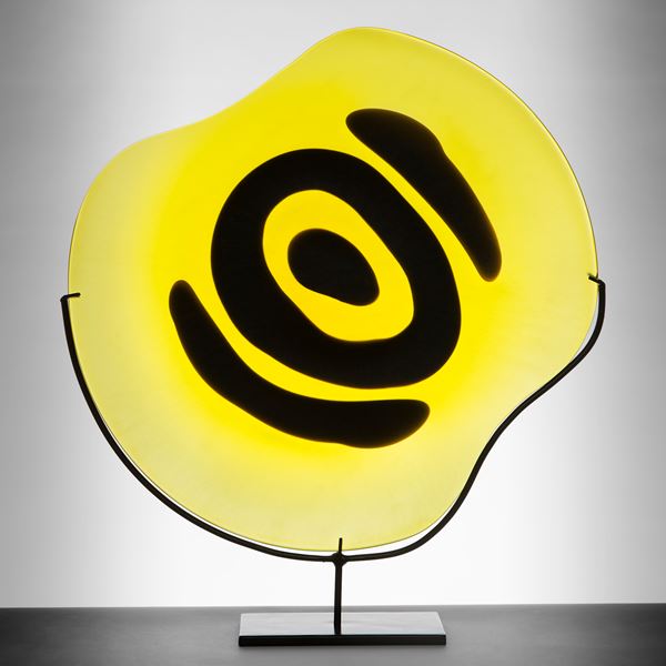 yellow rounded glass sculpture with black painted eye on metal stand