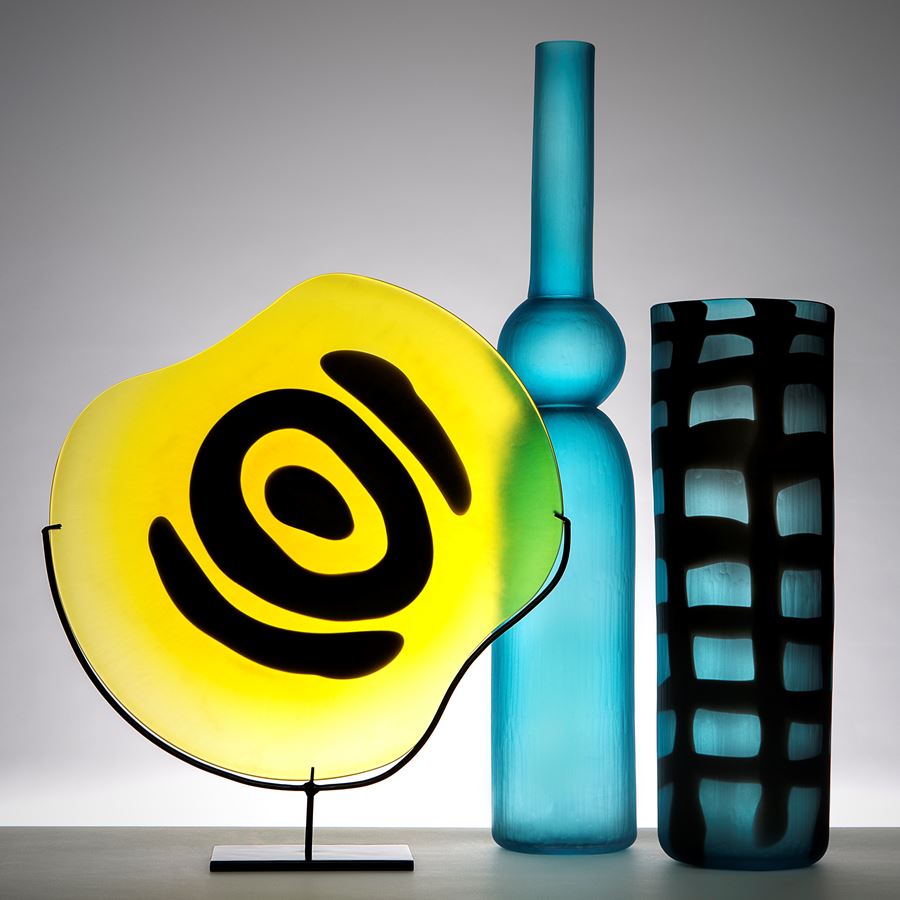 yellow rounded glass sculpture with black painted eye on metal stand