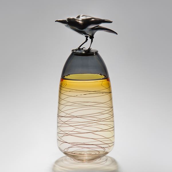 glass and steel sculpture of a crow atop a clear and yellow tinted vase with helter skelter pattern