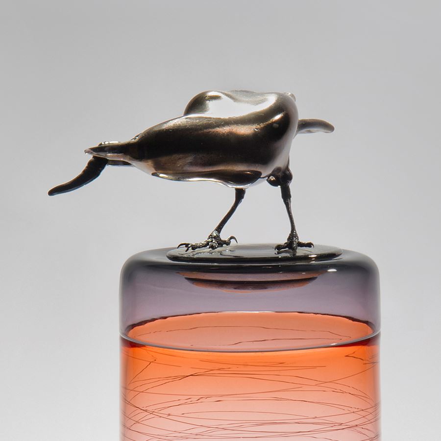 sculpted glass vase in clear and orange with faint lines encircling exterior with stainless steel crow on top 