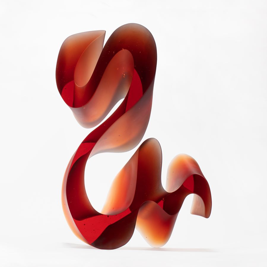amber red fluid lined sculpture with dramatic sweeping curves made from cast glass