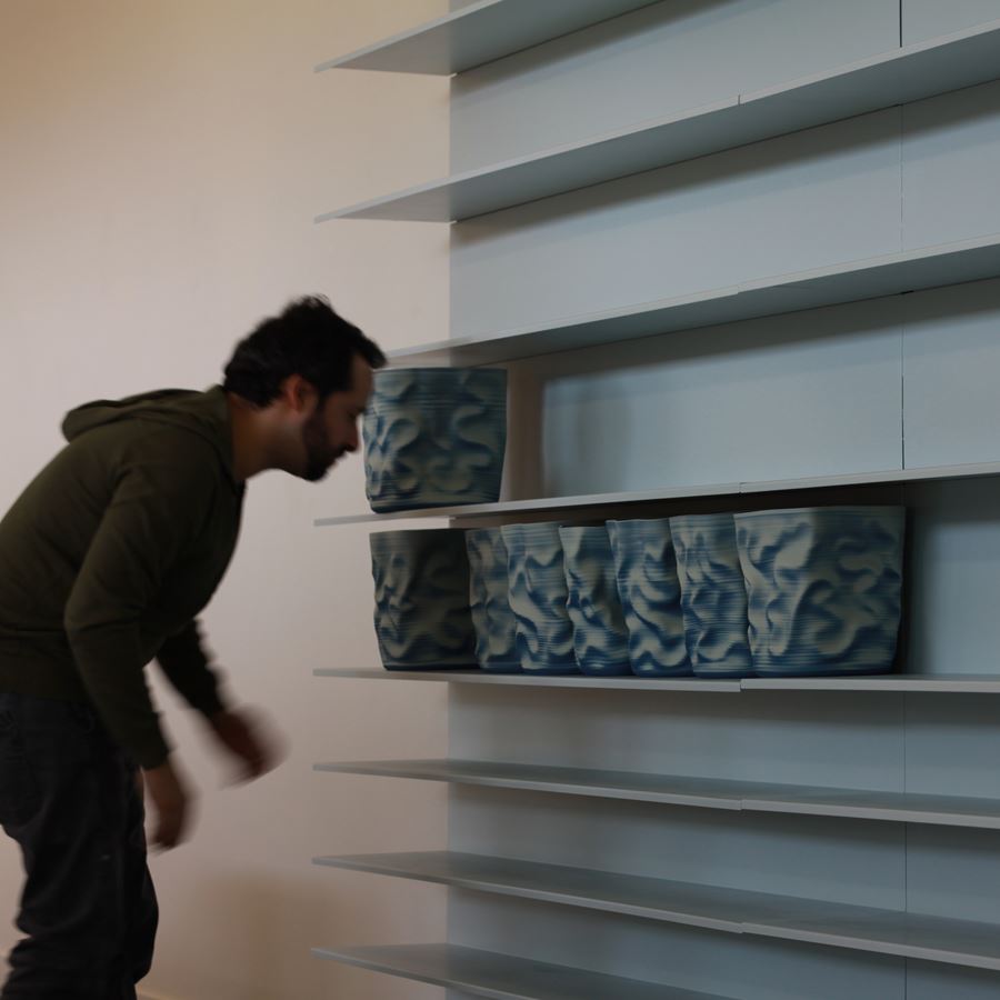 shelves of blue and cream scrunched and wrinkled looking hand thrown ceramic vessels creating a large wall mounted sculptural installation